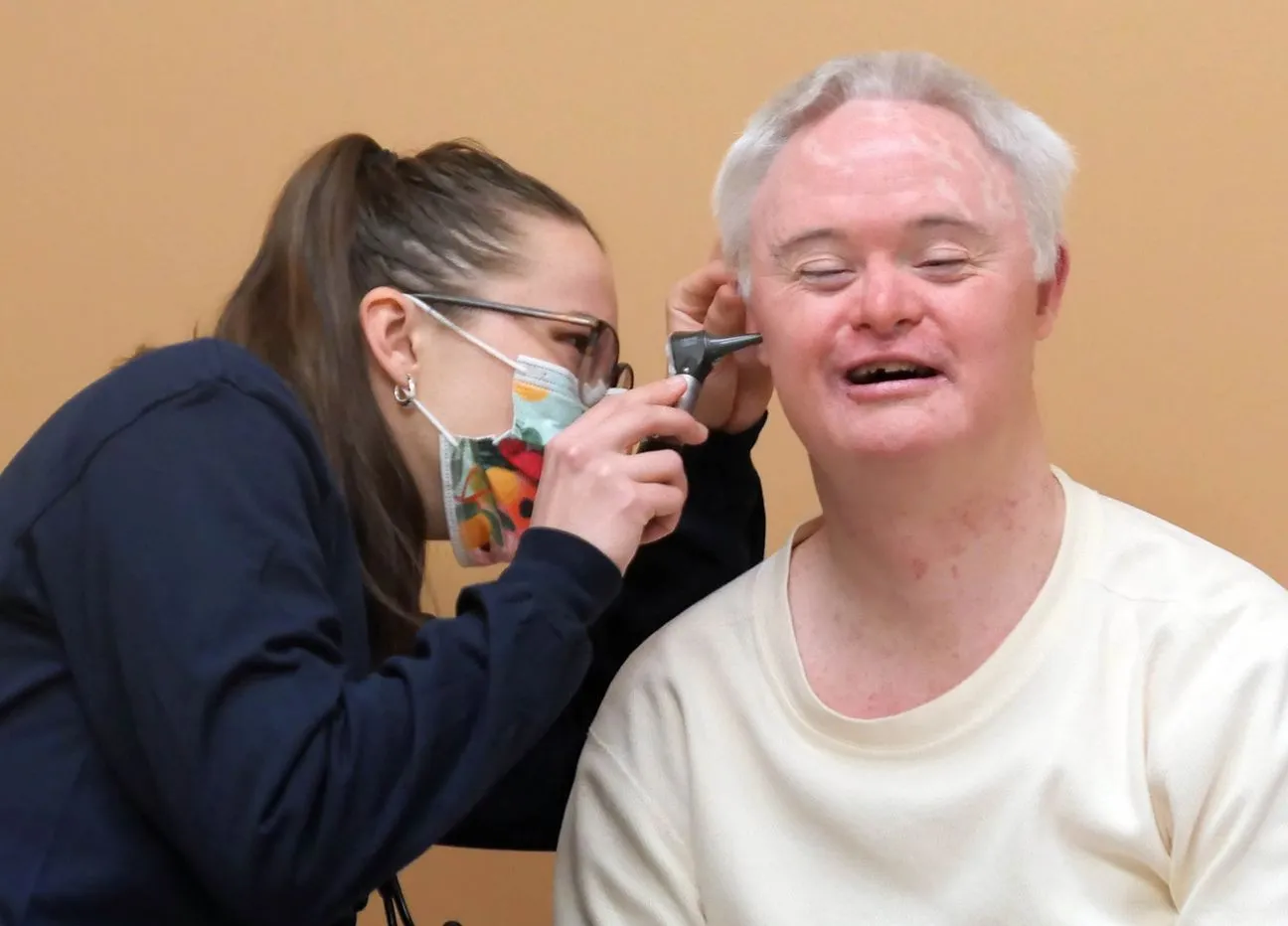 Female doctor wearing a face mask and eyeglasses checking a male patient's ear.