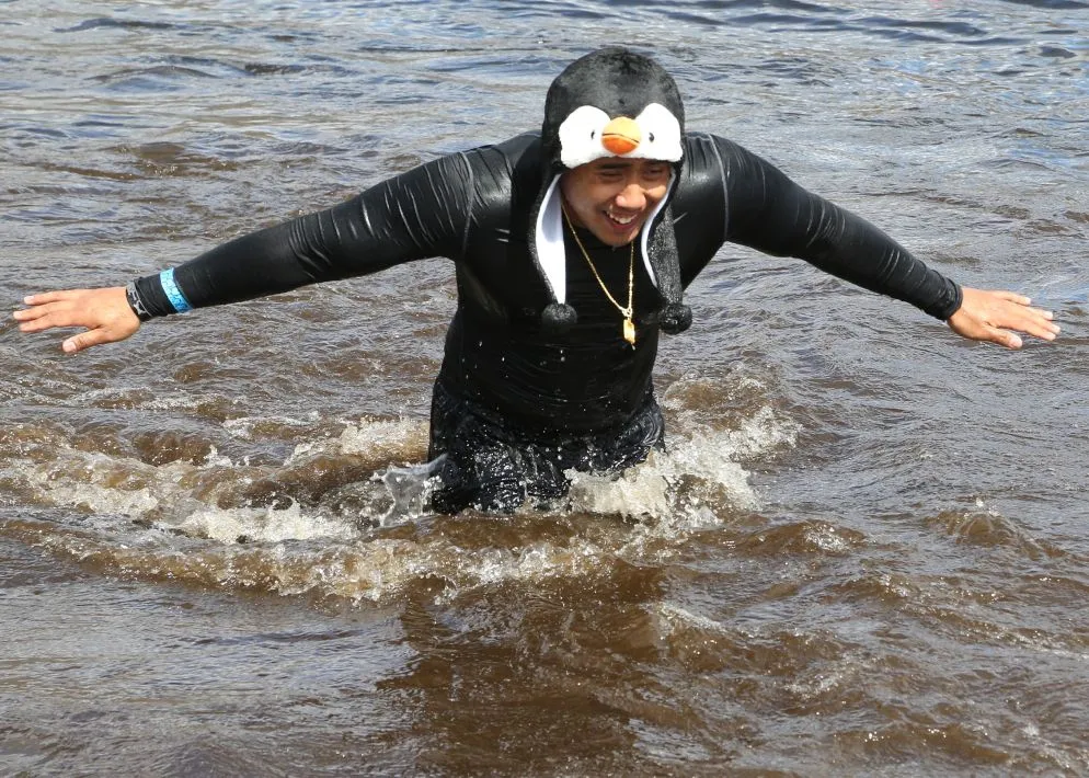 Young adult athlete wearing a black swim suit and a penguin hat running in the water.