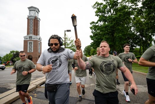 Man carrying torch wearing a black torch run shirt jogging with others.