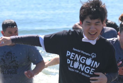 Young athletes running in the water participating in the Penguin Plunge.