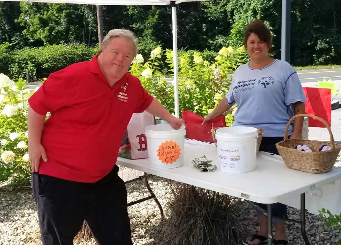 Two adults standing under a tent at a table with money and buckets on it collecting donations.