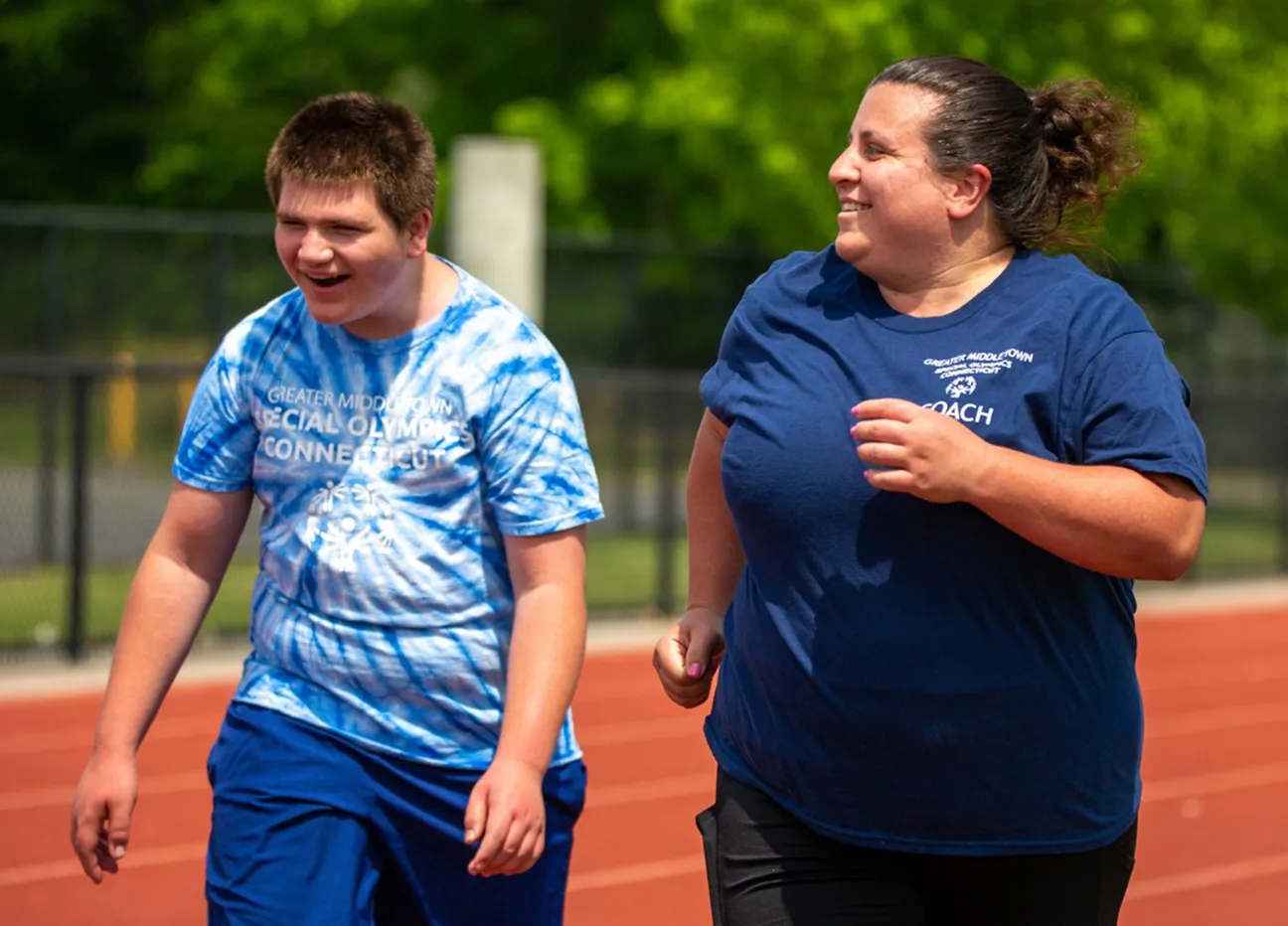 Coach and athlete running side-by-side wearing blue t-shirts on a track.
