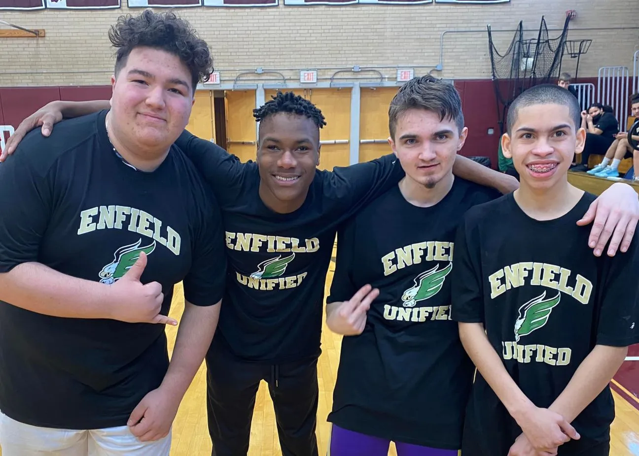 Group of four young adults wearing Enfield Unified shirts posing together.